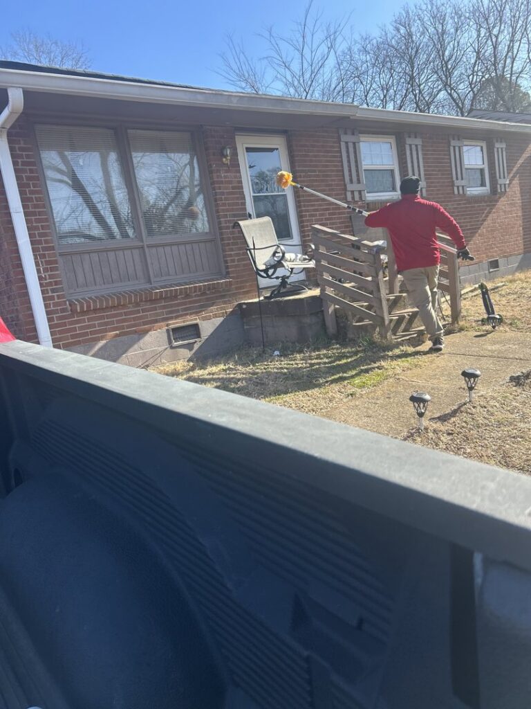 A pest control technician treating the exterior of a house with a long pole for pest management by DOA Pest Service in Nashville, TN.