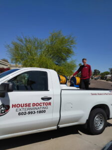 A pest control technician standing next to a House Doctor Exterminating truck with equipment in Glendale, AZ.