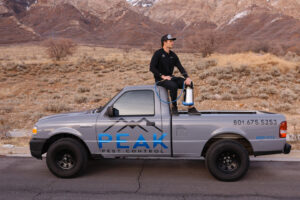 A Peak Pest Control technician sitting on the back of a branded truck with a sprayer, ready for service in Ogden, UT.