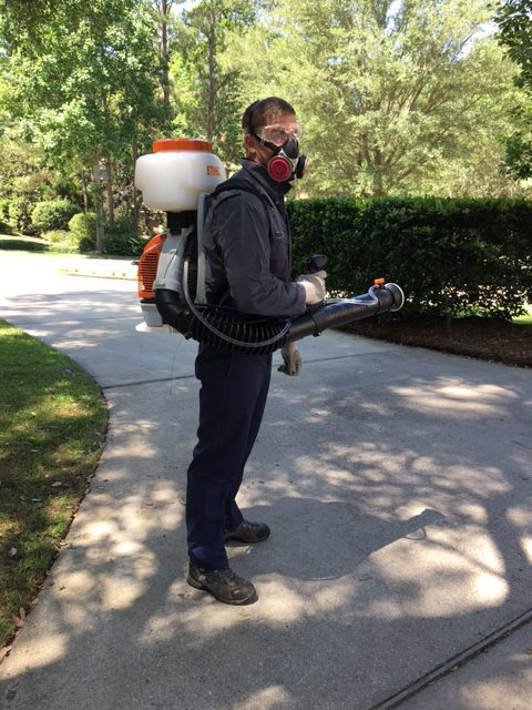 A pest control technician wearing a respirator mask and using a backpack sprayer at All-Around Termite and Pest Control in Tallahassee, FL.