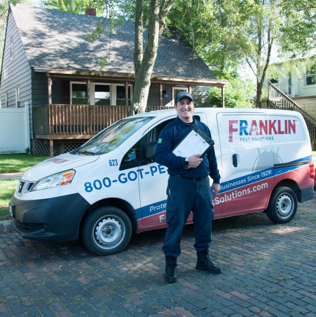 A pest control technician in uniform standing proudly next to a Franklin Pest Solutions van in Lafayette, IN.