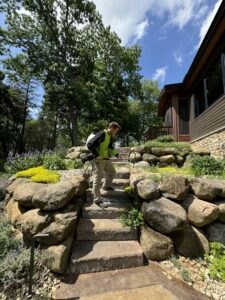 A Green Harmony pest control technician walking with equipment on a residential job site in Oconomowoc, WI.