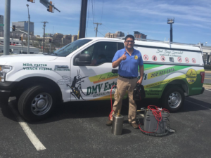 A pest control technician standing with equipment next to a branded truck for El Exterminador Del DMV in Rockville, MD.