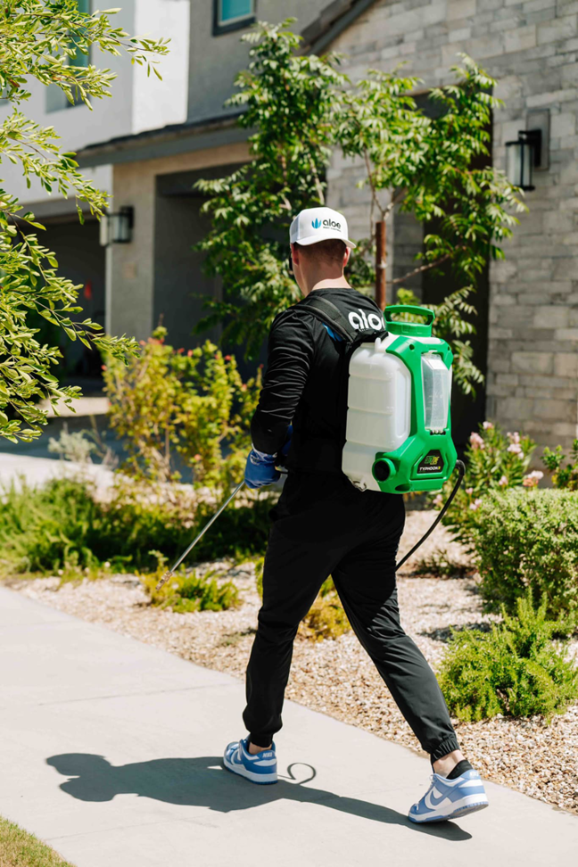 A pest control technician from Aloe Pest Control walking with a backpack sprayer during service in Mesa, AZ.