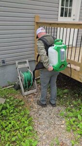 A pest control technician from Titan Pest Pro - Springfield with a backpack sprayer near a residential house in Springfield, MO.