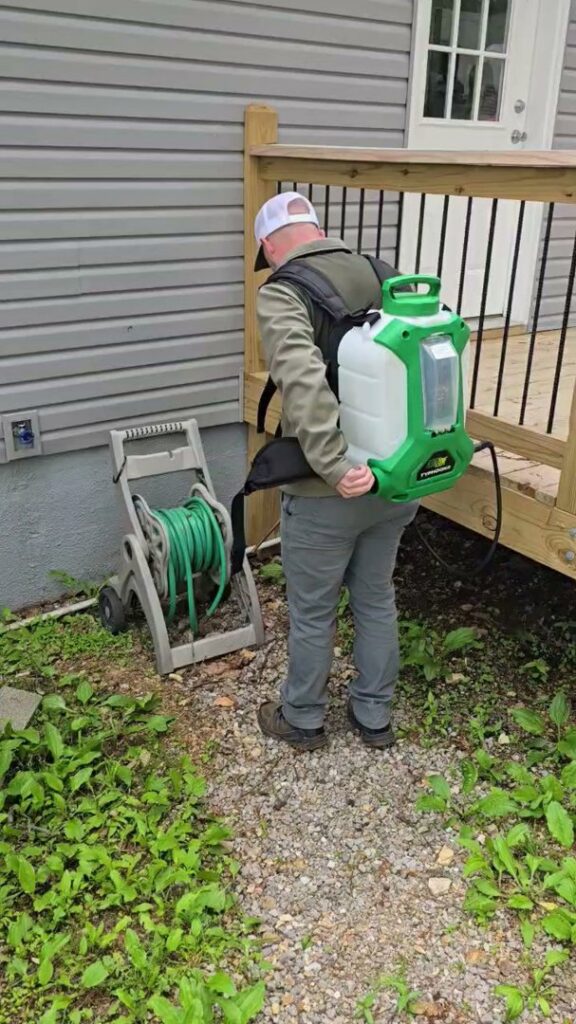 A pest control technician from Titan Pest Pro - Springfield with a backpack sprayer near a residential house in Springfield, MO.