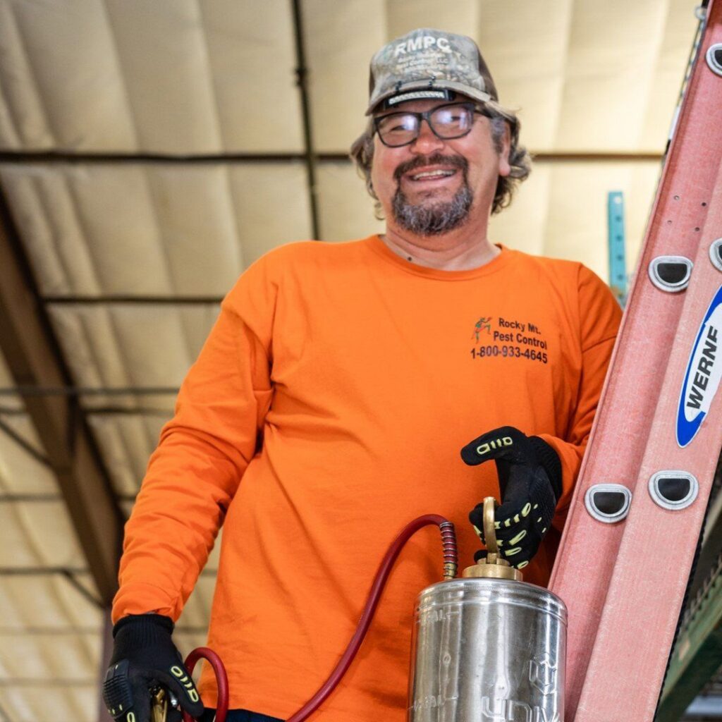 A pest control technician from Rocky Mountain Pest Control in Santa Fe, NM, holding a sprayer and standing next to a ladder, ready for service.