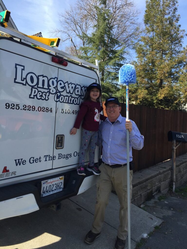 A Longeway Pest Control technician holding a long pest removal tool next to a branded truck in Oakland, CA.