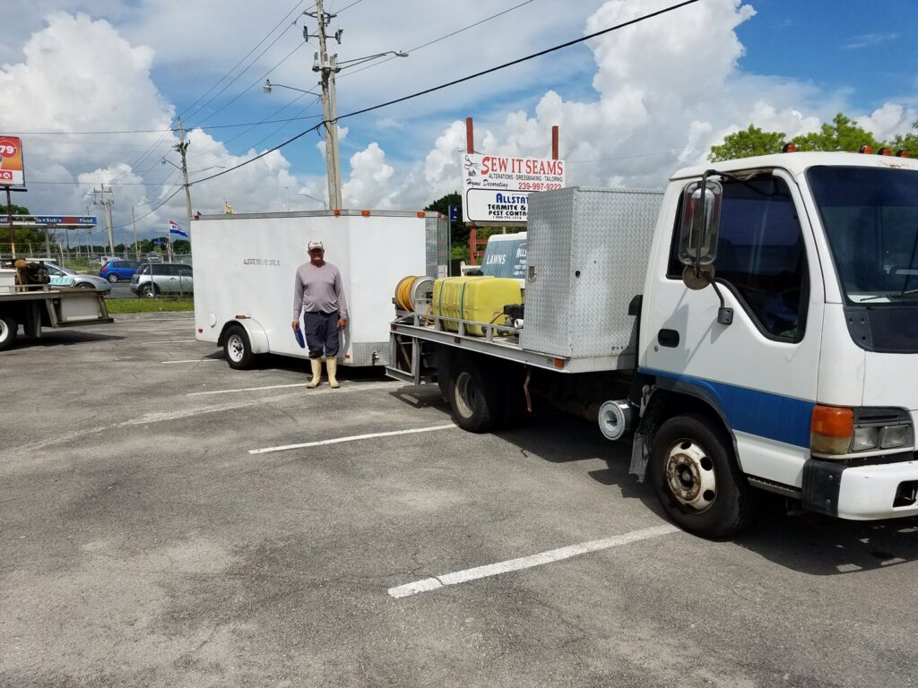 A pest control technician standing with a service truck and trailer from Allstate Termite and Pest Control Inc. in Tampa, FL.