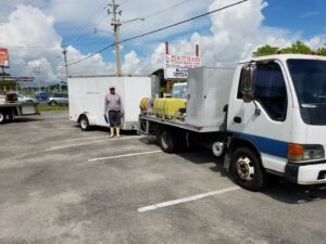A pest control technician standing with a service truck and trailer from Allstate Termite and Pest Control Inc. in Tampa, FL.