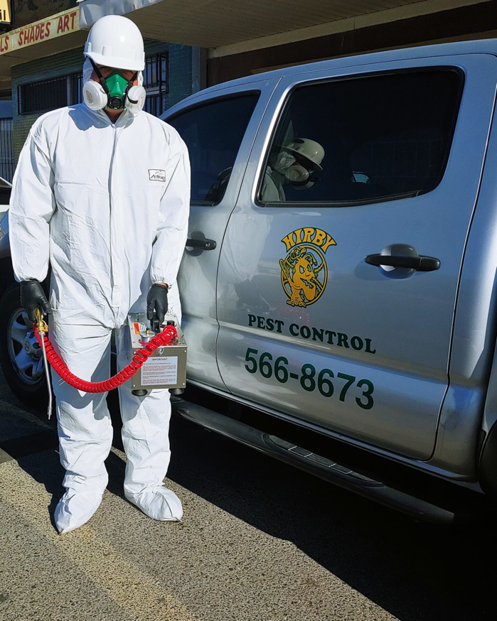 A pest control technician in protective gear standing by a Hirby Pest Control truck in El Paso, TX