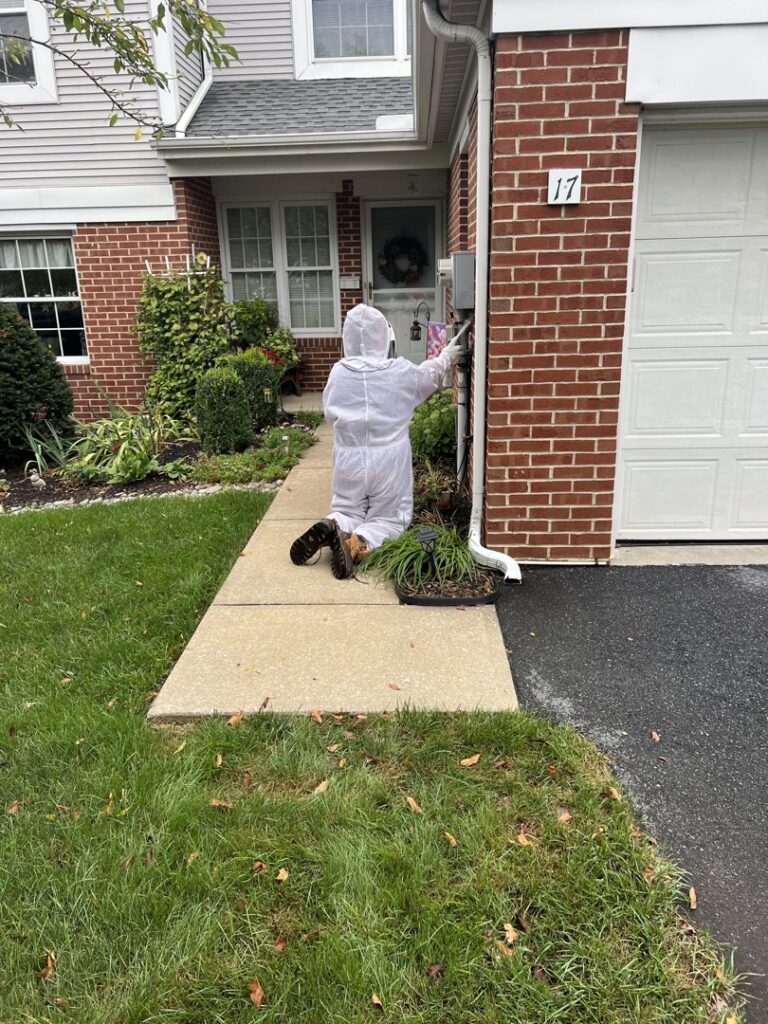 A pest control technician in protective gear kneeling to treat a home's foundation for Genesis Termite and Pest Control in New Holland, PA.