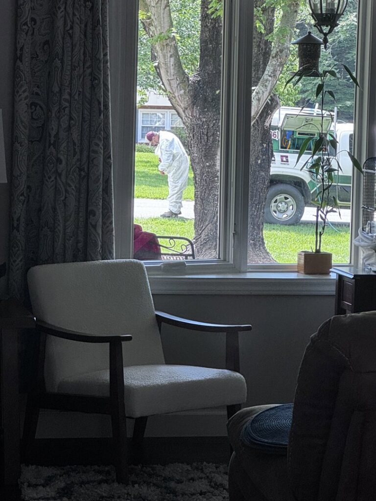 A Bulwark Exterminating technician in a white suit performing pest control services outside a home in Greensboro, NC.