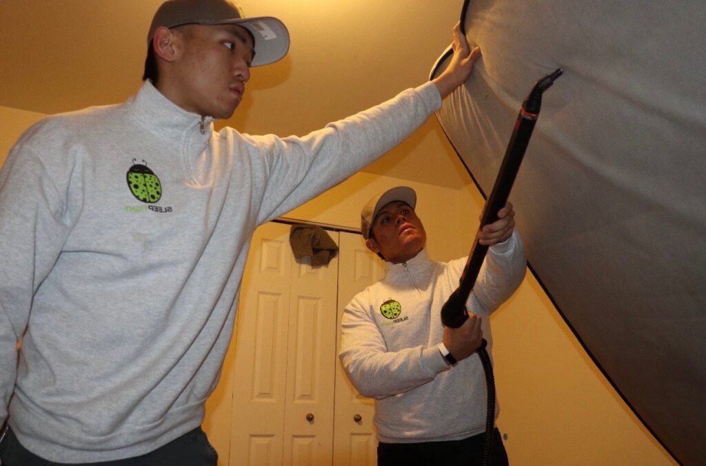 Two Sleep Tight Pest Control technicians inspecting a mattress or furniture for pests in Kansas City, KS.