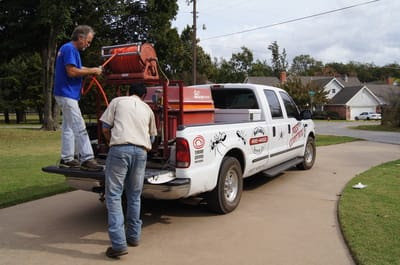 Two pest control technicians loading equipment onto a branded truck for Reliable Termite of OKC in Oklahoma City, OK.