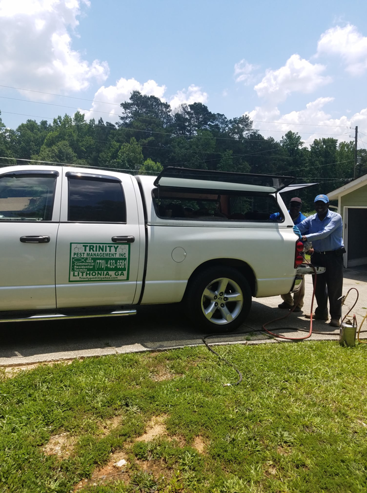 Trinity Pest Management, Inc. technicians preparing equipment for a pest control service next to their company truck in Redan, GA.