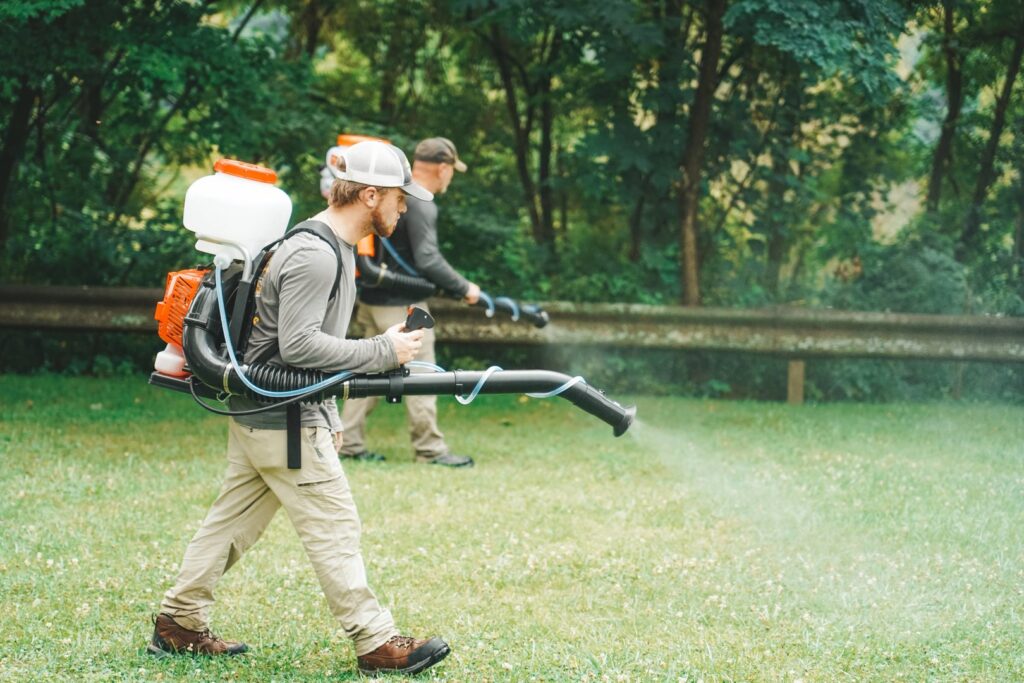 Two pest control technicians spraying a residential yard with backpack sprayers for pest treatment at Complete Pest Solutions of Canton in North Canton, OH.