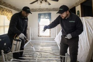 Two Sleep Tight Pest Control technicians treating a bed frame for pests in a home in Kansas City, KS.