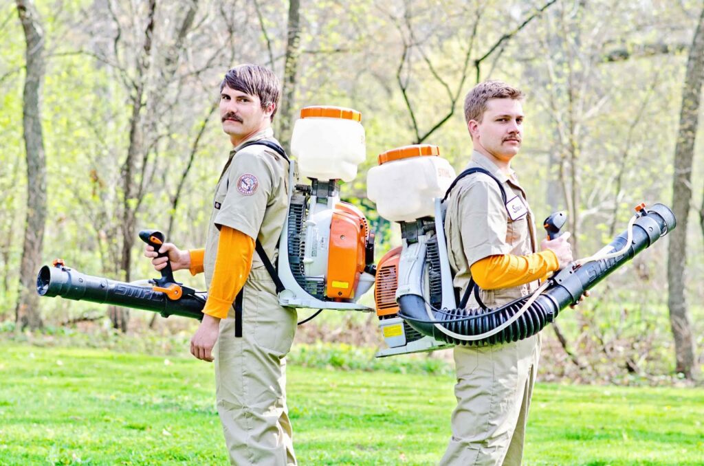 Two pest control technicians wearing uniforms and backpack sprayers for Mosquito Hunters of Grand Rapids, MI.
