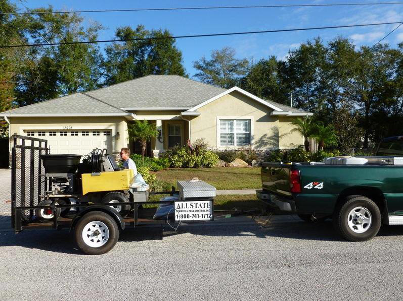 A pest control truck and trailer with equipment parked at a residential job site by Allstate Termite and Pest Control Inc. in Tampa, FL.