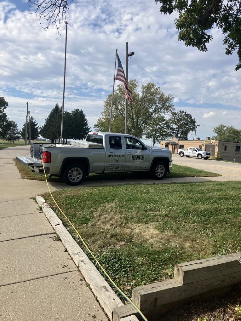 A Modern Solutions Pest Control truck with a hose extended, ready for or performing pest treatment in Rockford, IL.