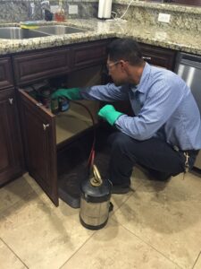 A Dan's Pest Management technician performing pest control under a kitchen sink in Bakersfield, CA