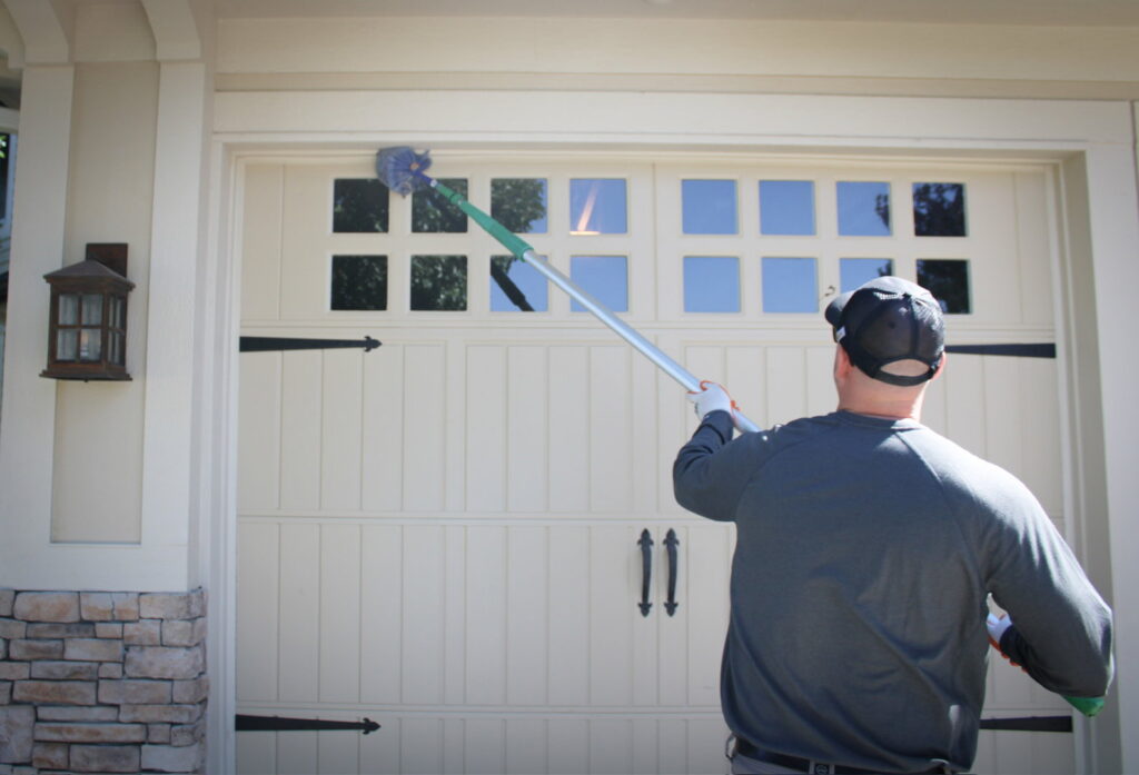 An Upfront Pest technician removing spiderwebs from above a garage door in North Kansas City, MO.