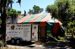 A pest control worker on the roof of a house covered in a fumigation tent, with a Rivers Pest Control trailer nearby in Jacksonville, FL