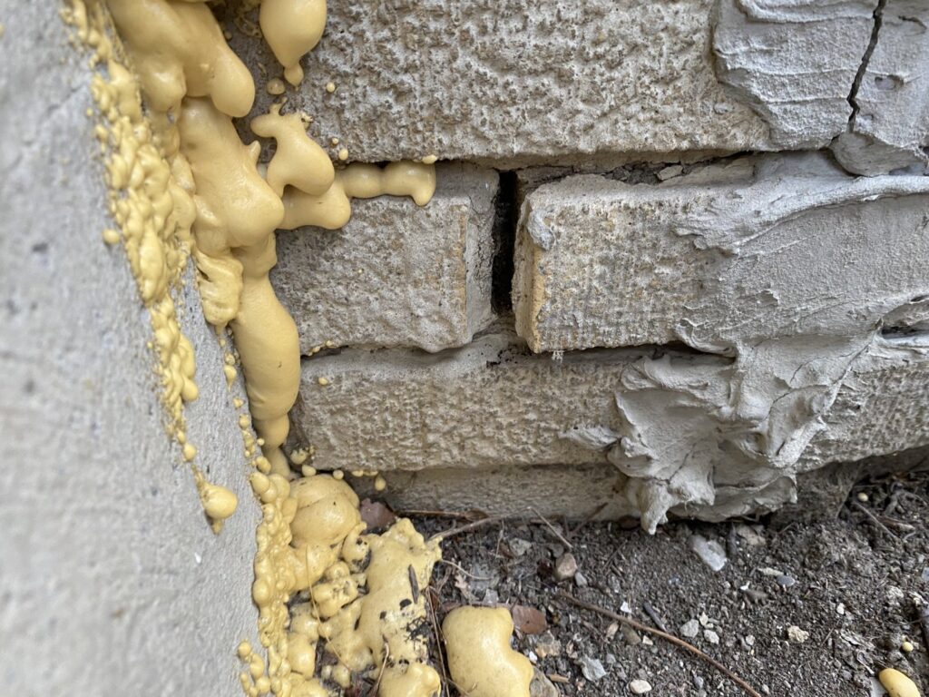 Expanding foam sealant applied to seal gaps in a stone foundation, demonstrating pest exclusion work by Moderno Pest Control in Fort Wayne, IN.