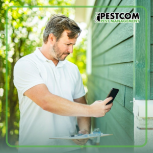 A Pestcom Pest Management technician performing a detailed pest inspection on the exterior of a home in Nampa, ID