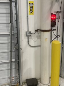 A yellow sign on a wall indicating a pest management device location inside a commercial building by Drapers Pest Management in Fort Worth, TX.