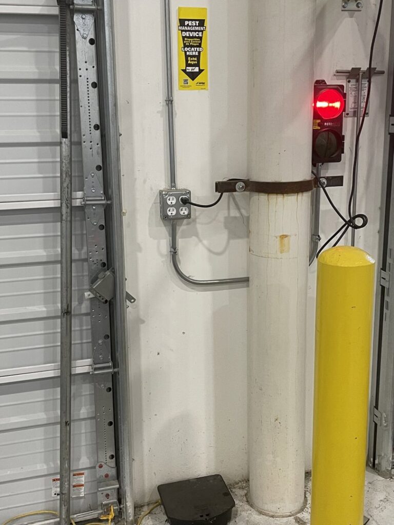 A yellow sign on a wall indicating a pest management device location inside a commercial building by Drapers Pest Management in Fort Worth, TX.