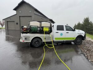 A Pest One service truck with hoses extended, performing pest control or plant health treatment on a driveway in Bozeman, MT.