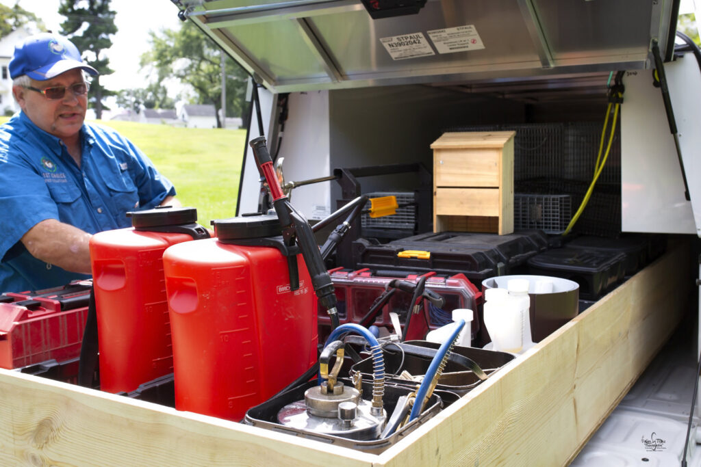 A pest control technician with a truck bed full of equipment, including sprayers and wildlife traps, for 1st Choice Pest Solutions in Eau Claire, WI.