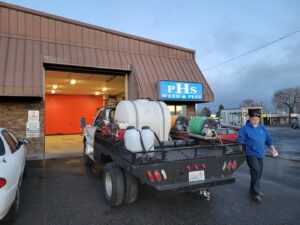 A PHS Weed & Pest Control technician near a service truck with pest control equipment in Spokane, WA.