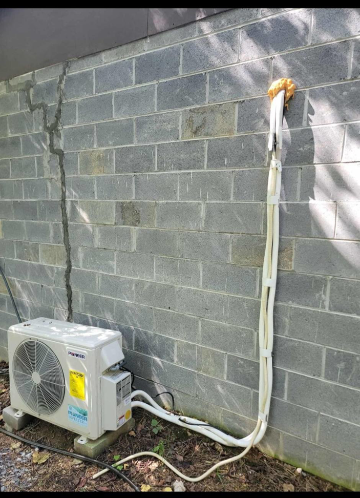 A Pioneer brand mini-split HVAC unit with refrigerant lines installed on a cinder block wall by Smoky Mountain Ducts & Vents in New Market, TN.