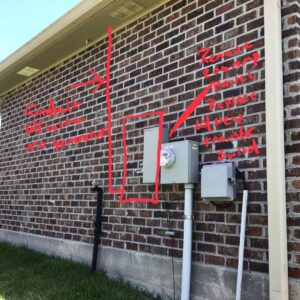A brick wall showing an electrical meter and conduit with red markings for planned generator service by Craig's Electrical and Generator Service in Kenner, LA.