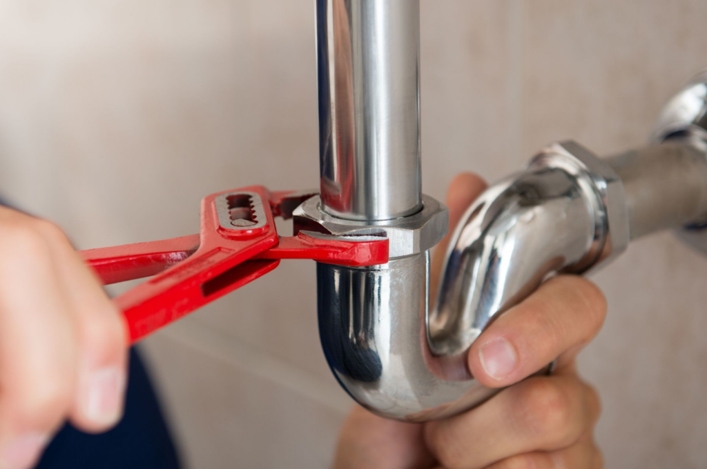 A plumber tightening a pipe connection with a wrench, demonstrating plumbing services by Sarca Services in Springfield, VA.