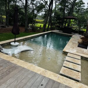 A swimming pool featuring a beach entry and surrounded by wood decking and pavers, a project by Salty Reef Pools LLC in Summerville, SC.