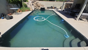 A swimming pool with a robotic cleaner and hose actively cleaning the water, demonstrating work by AZ Pool Love in Mesa, AZ