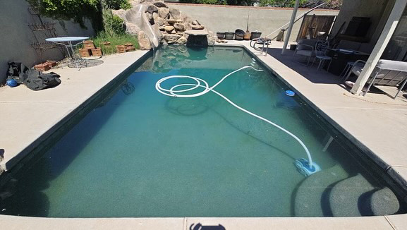 A swimming pool with a robotic cleaner and hose actively cleaning the water, demonstrating work by AZ Pool Love in Mesa, AZ