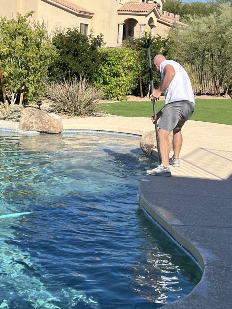 A pool cleaner from The Good Pool Company brushing the pool with a long pole in Scottsdale, AZ.