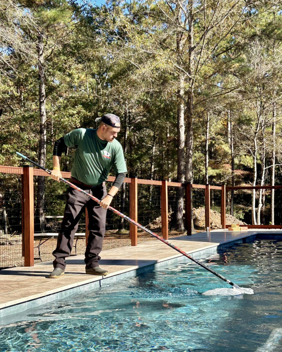 A professional pool cleaner from Freedom Pools skimming leaves and debris from a residential pool in Austin, TX.