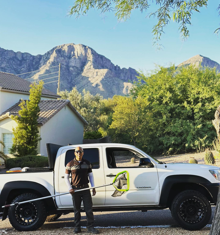 A professional pool cleaner from Az Pool Man in Tucson, AZ, holding a skimmer net next to a service truck.