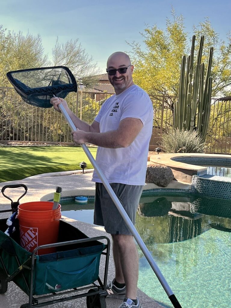 A pool cleaner from The Good Pool Company holding a skimmer net next to a pool in Scottsdale, AZ.