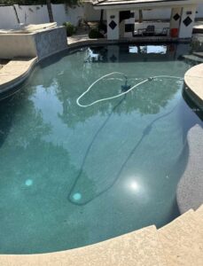 A swimming pool with a cleaning hose actively working, showing pool cleaning in progress by Pool Pals in Franklin, MA.
