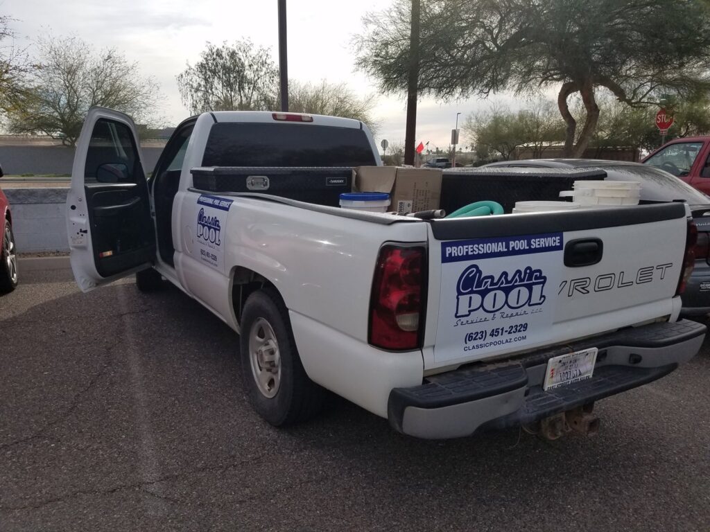 Various pool cleaning tools and supplies laid out next to a clean pool by Classic Pool Service in Surprise, AZ