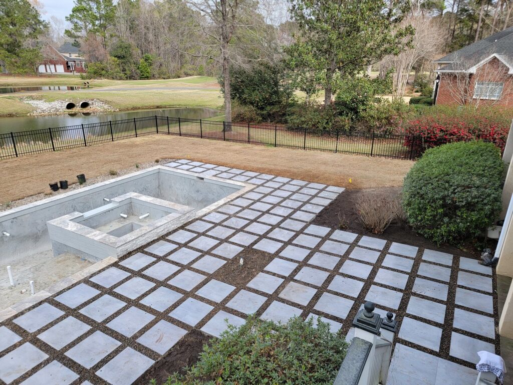 A swimming pool under construction with the concrete shell visible and patio pavers being installed by Salty Reef Pools LLC in Summerville, SC.