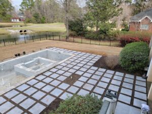 A swimming pool under construction with the concrete shell visible and patio pavers being installed by Salty Reef Pools LLC in Summerville, SC.