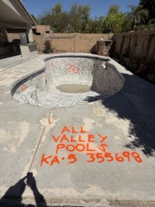An empty pool construction site with markings for All Valley Pools in Avondale, AZ, indicating work in progress.